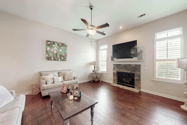 living area with baseboards, a ceiling fan, a stone fireplace, and visible vents