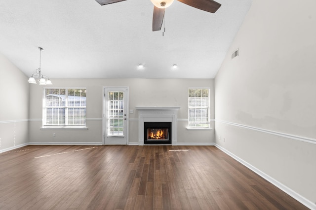 unfurnished living room featuring ceiling fan with notable chandelier, a wealth of natural light, dark hardwood / wood-style floors, and vaulted ceiling