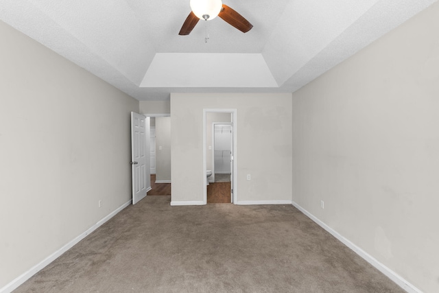 unfurnished bedroom featuring a walk in closet, carpet floors, a closet, ceiling fan, and a tray ceiling