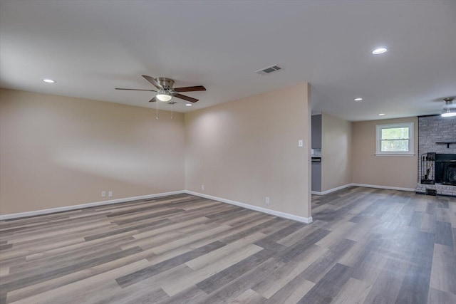 interior space with a brick fireplace, ceiling fan, and light wood-type flooring