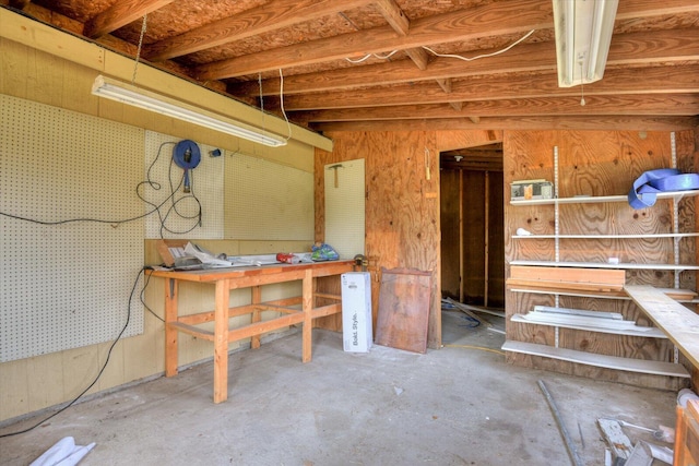 misc room featuring a workshop area, wooden walls, and concrete floors