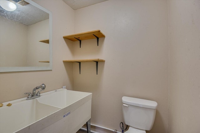 bathroom featuring a textured ceiling, toilet, and sink