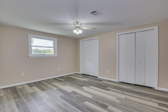 unfurnished bedroom with ceiling fan, light hardwood / wood-style flooring, and two closets