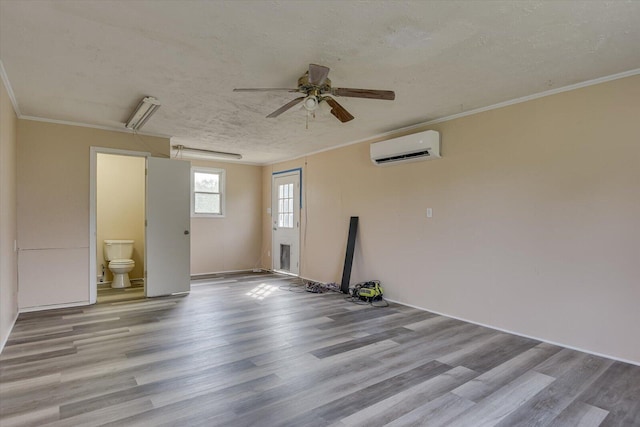 empty room featuring a wall unit AC, ceiling fan, ornamental molding, and light wood-type flooring