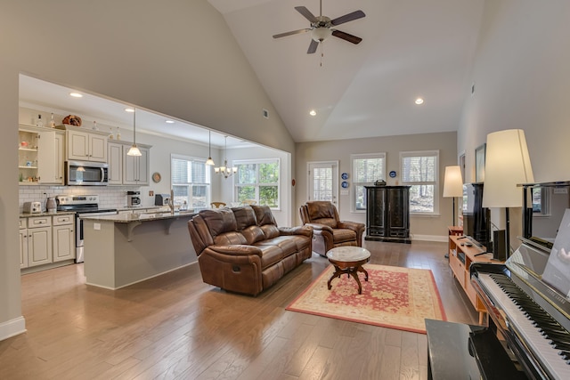 living area featuring baseboards, ceiling fan with notable chandelier, light wood-type flooring, high vaulted ceiling, and recessed lighting