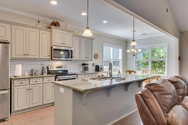 kitchen with appliances with stainless steel finishes, hanging light fixtures, an island with sink, and light stone counters