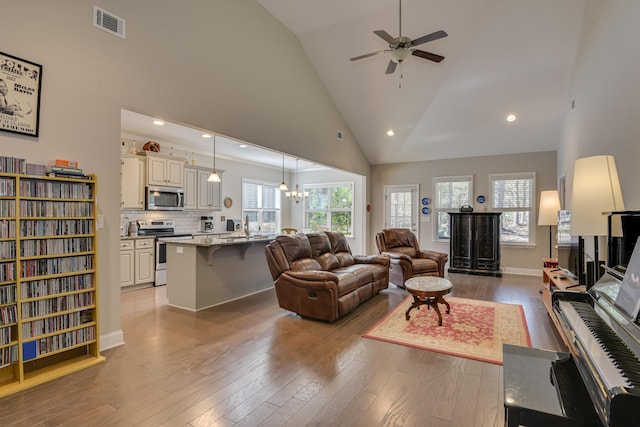 living room with high vaulted ceiling, ceiling fan with notable chandelier, visible vents, baseboards, and light wood-style floors