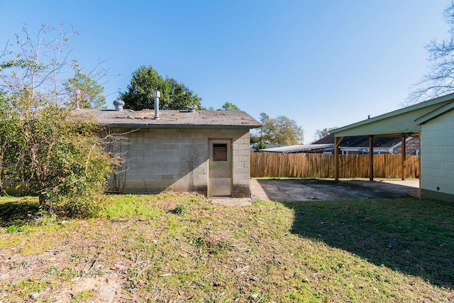 back of house with concrete block siding, fence, a lawn, and a patio area