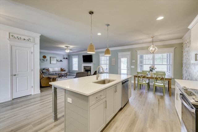 kitchen with sink, white cabinets, hanging light fixtures, stainless steel appliances, and a center island with sink