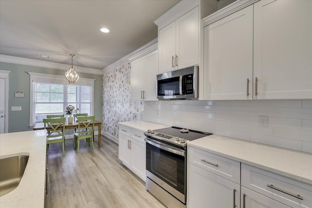 kitchen with crown molding, appliances with stainless steel finishes, light stone counters, white cabinets, and decorative light fixtures