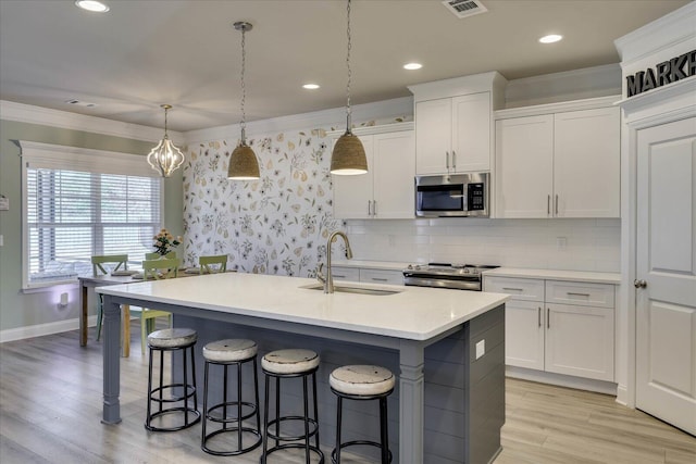 kitchen featuring sink, a kitchen island with sink, hanging light fixtures, stainless steel appliances, and white cabinets