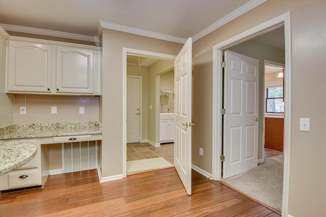 kitchen with light stone countertops, built in desk, white cabinetry, and crown molding