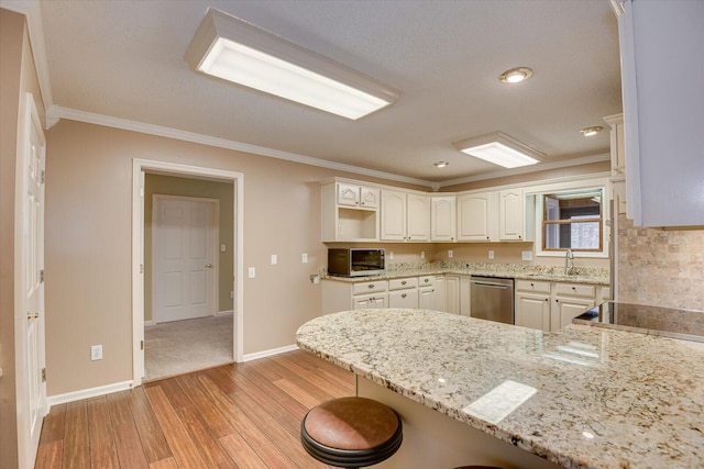 kitchen featuring kitchen peninsula, stainless steel dishwasher, light stone counters, white cabinetry, and a breakfast bar area