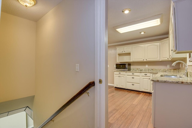 kitchen featuring white cabinets, crown molding, sink, light stone countertops, and light hardwood / wood-style floors