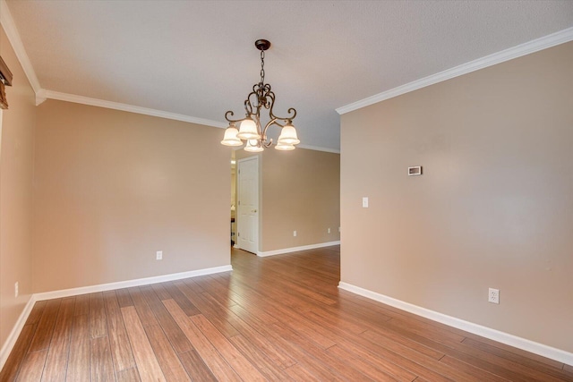 spare room with hardwood / wood-style floors, crown molding, and an inviting chandelier