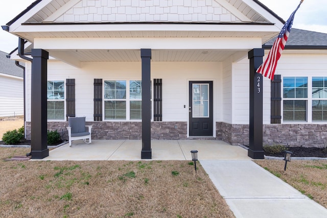 entrance to property with a porch, stone siding, and roof with shingles