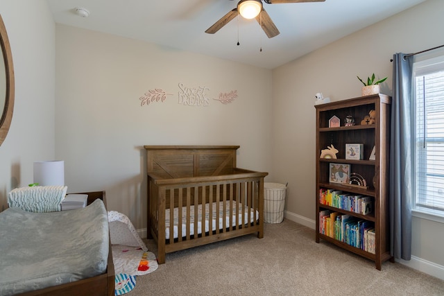 carpeted bedroom with ceiling fan, a crib, and baseboards