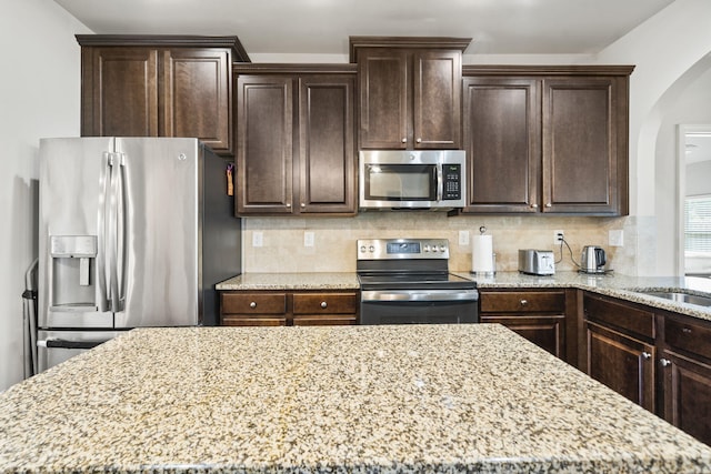 5315 Bull St, Augusta, GA 30909 - kitchen with appliances with stainless steel finishes, arched walkways, light stone counters, a kitchen island, and backsplash