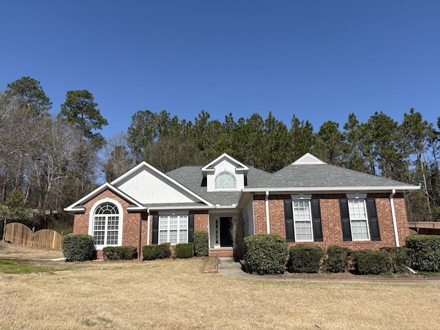 view of front facade with brick siding, a shingled roof, a front lawn, and fence