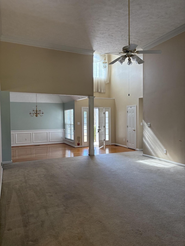 unfurnished living room featuring crown molding, ceiling fan with notable chandelier, and carpet floors