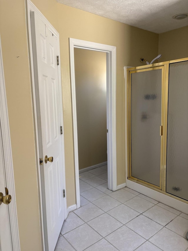 full bath featuring tile patterned flooring, baseboards, a stall shower, and a textured ceiling