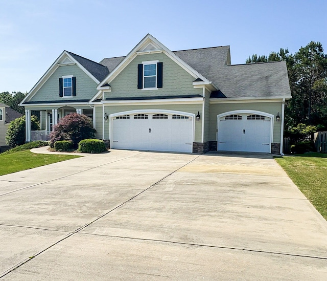 craftsman inspired home with an attached garage, a front lawn, roof with shingles, and driveway