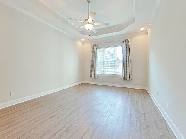 empty room featuring a ceiling fan, a tray ceiling, ornamental molding, and light wood-style flooring