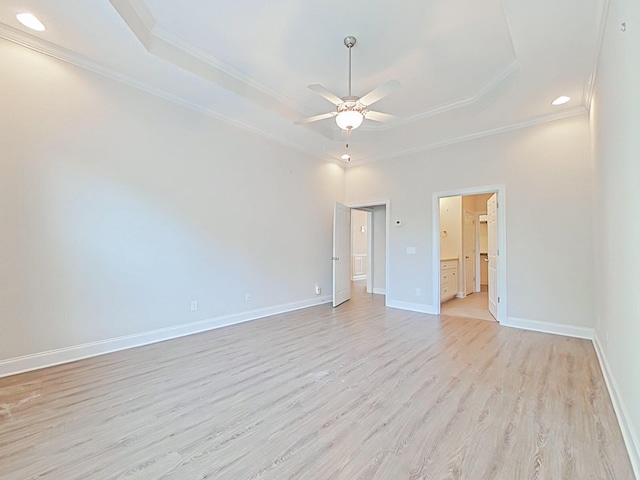 spare room featuring ceiling fan, light wood-type flooring, baseboards, ornamental molding, and a tray ceiling