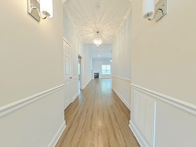 corridor featuring visible vents, wood finished floors, baseboards, an inviting chandelier, and ornamental molding