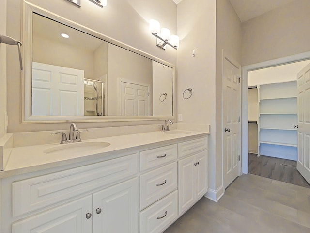 bathroom featuring double vanity, a sink, wood finished floors, and a shower stall