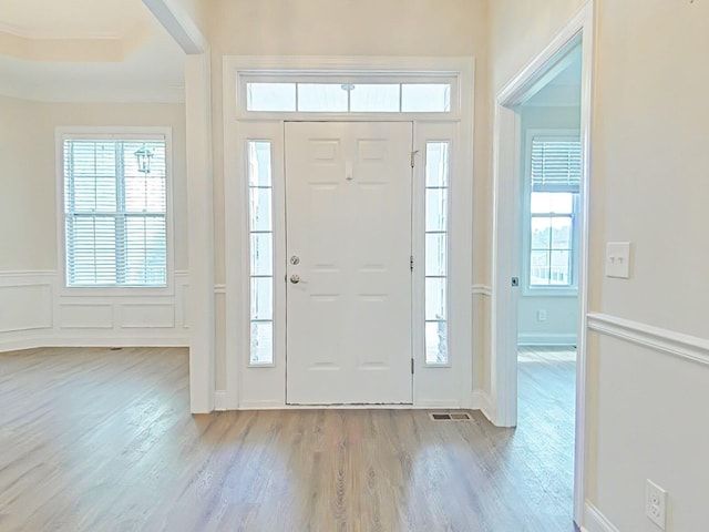 foyer entrance featuring a wainscoted wall, a decorative wall, wood finished floors, and visible vents