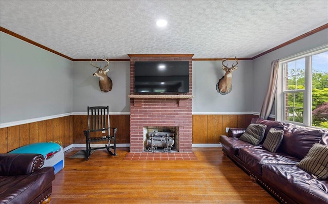 living area with a textured ceiling, wood finished floors, a fireplace, and wainscoting