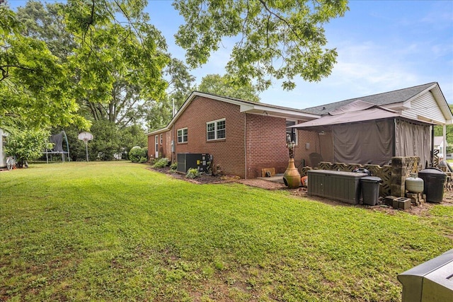 rear view of house featuring a yard, central AC, a trampoline, and brick siding