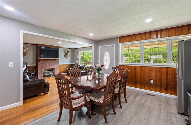 dining space featuring light wood finished floors, wooden walls, a fireplace, and a textured ceiling