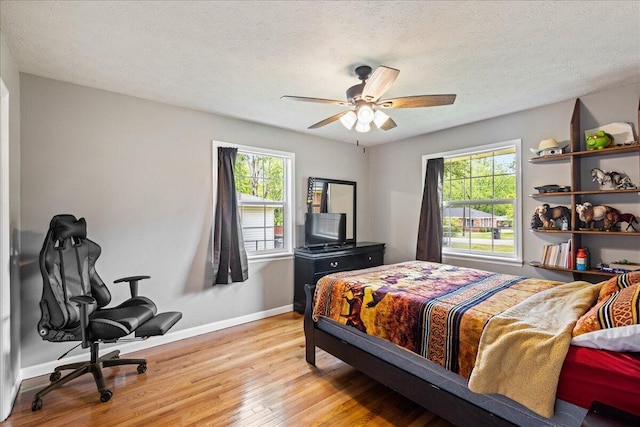 bedroom with multiple windows, baseboards, light wood-type flooring, and a textured ceiling