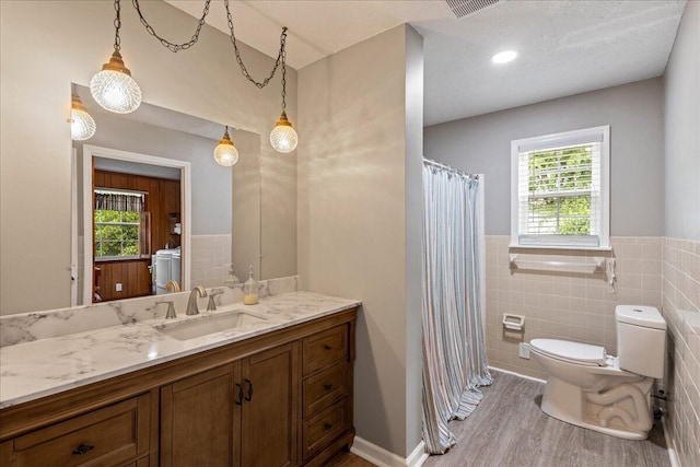 bathroom with toilet, wood finished floors, tile walls, washer / dryer, and vanity