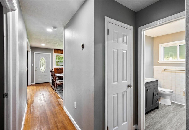 corridor featuring a wainscoted wall, tile walls, light wood-type flooring, and a textured ceiling