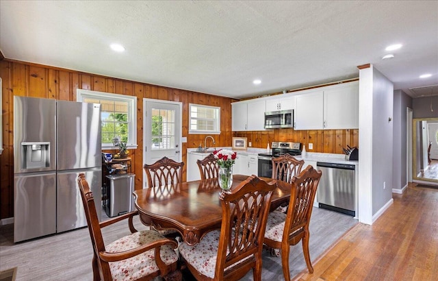 dining area with a textured ceiling, wooden walls, recessed lighting, and light wood finished floors