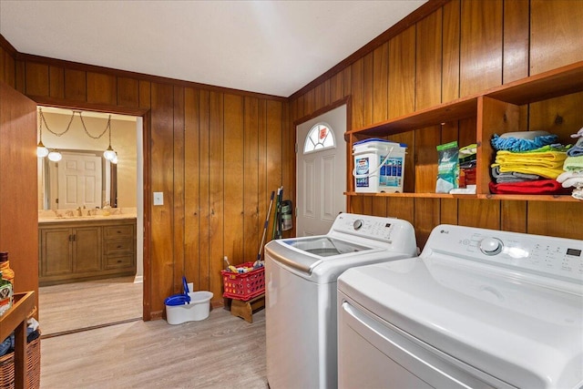 laundry room featuring wooden walls, laundry area, separate washer and dryer, a sink, and light wood-type flooring