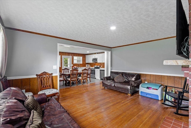 living room with a textured ceiling, wood finished floors, wooden walls, wainscoting, and crown molding