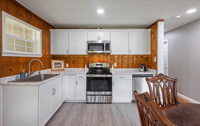 kitchen with wooden walls, light wood finished floors, a sink, stainless steel appliances, and white cabinetry