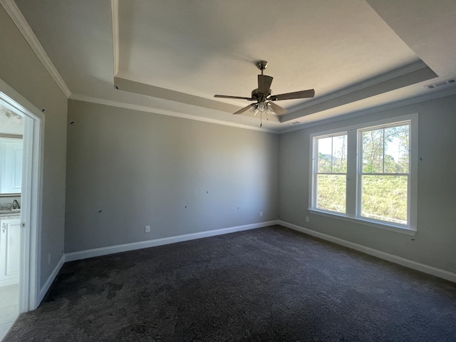 empty room with ceiling fan, dark carpet, ornamental molding, and a tray ceiling