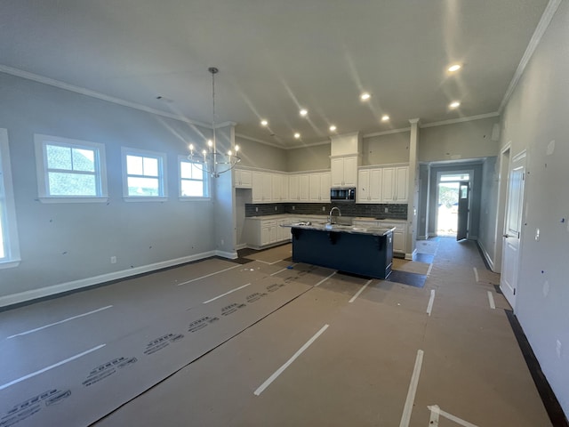 kitchen with pendant lighting, backsplash, a center island with sink, white cabinets, and sink