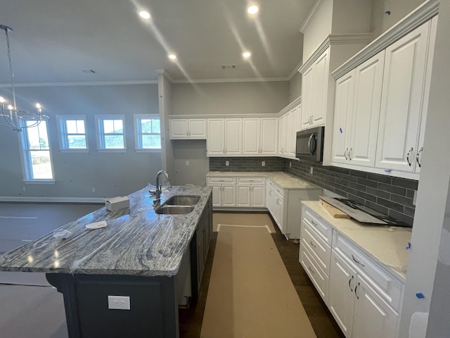 kitchen featuring crown molding, sink, light stone countertops, an island with sink, and white cabinetry