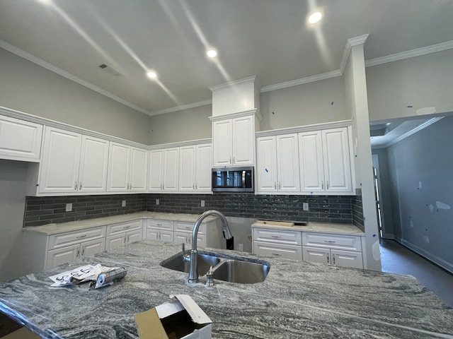 kitchen with light stone countertops, sink, tasteful backsplash, white cabinets, and ornamental molding