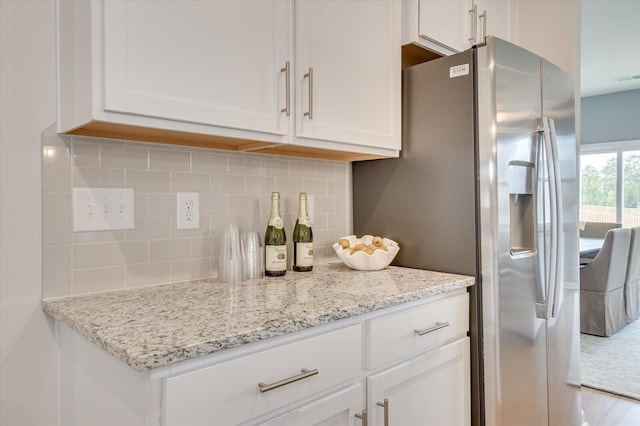 kitchen with backsplash, stainless steel fridge, light stone countertops, and white cabinets