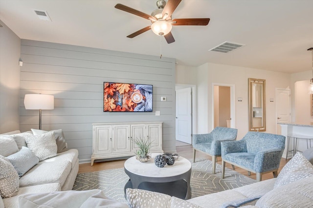 living room featuring hardwood / wood-style flooring, ceiling fan, and wooden walls