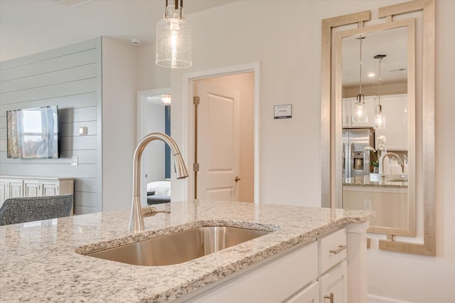 kitchen featuring light stone countertops, stainless steel refrigerator with ice dispenser, sink, decorative light fixtures, and white cabinets