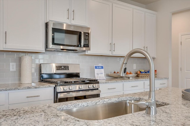 kitchen with decorative backsplash, white cabinetry, light stone countertops, and appliances with stainless steel finishes