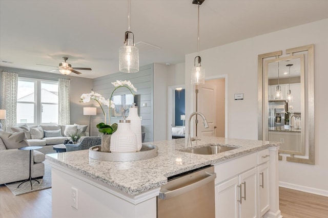 kitchen with stainless steel dishwasher, ceiling fan, sink, white cabinets, and an island with sink